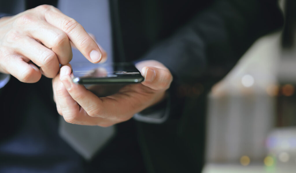 Closeup view of businessman hand using smartphone while standing outdoors at night.