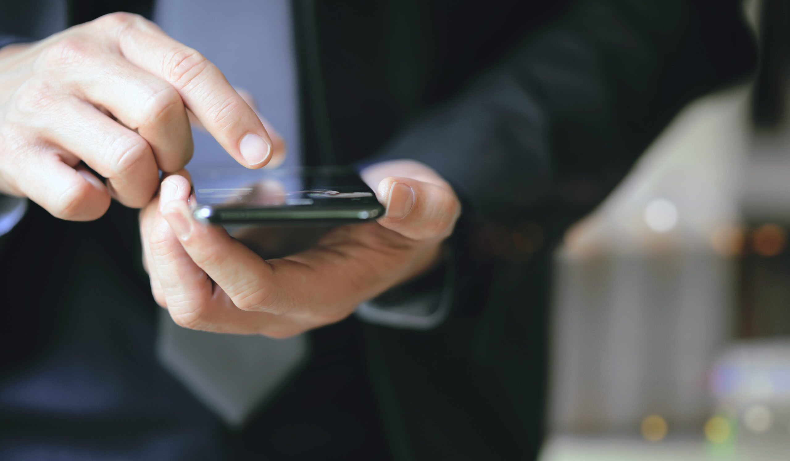 Closeup view of businessman hand using smartphone while standing outdoors at night.